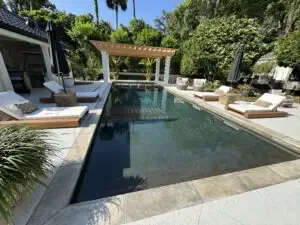Aerial view of a single-story house in a residential area featuring a screened-in pool on the side and a manicured yard with palm trees