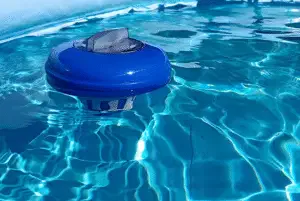 Close-up of a blue and white floating chlorine dispenser bobbing in bright, rippling swimming pool water for sanitization