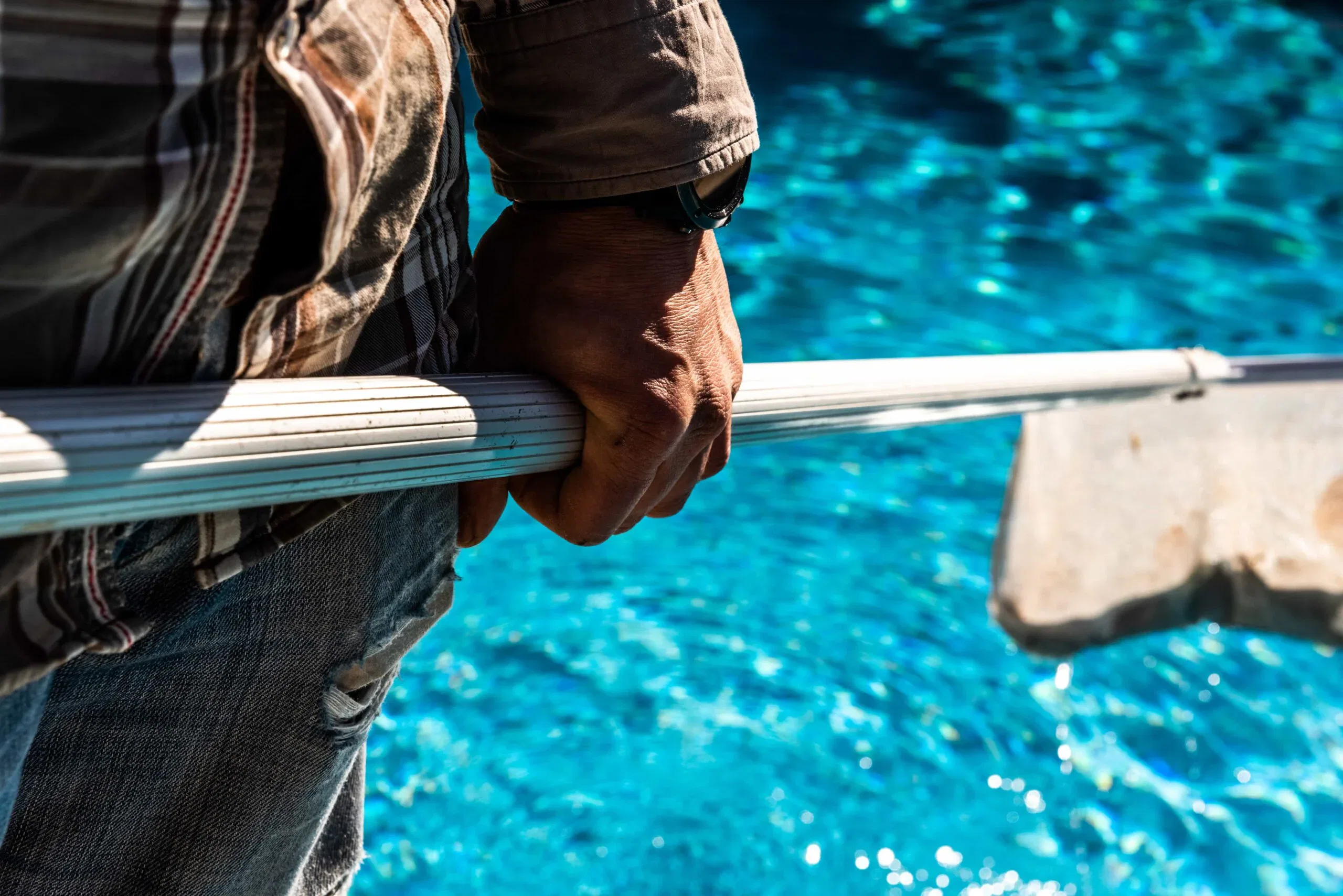 A pool maintenance technician using a leaf skimmer rake to clear debris from a residential swimming pool in Orlando, Florida.