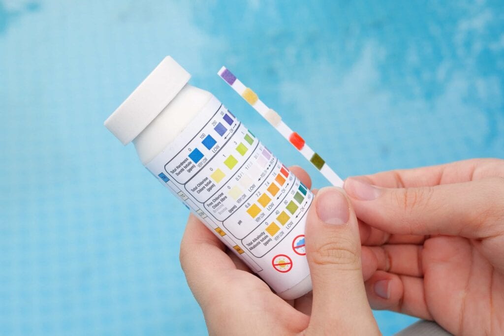 Close-up of a technician's hands comparing a pool water test strip to a color chart to check pH and chlorine balance in Orlando, Florida.