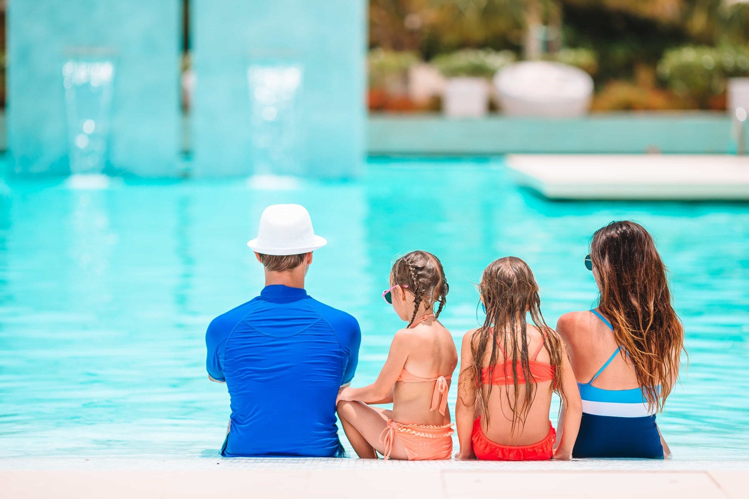 A happy family of four sitting by the edge of an outdoor luxury swimming pool in Scottsdale, AZ, enjoying a sunny day.