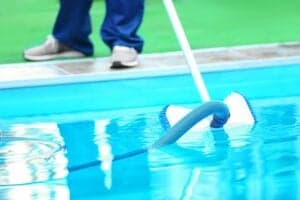 A worker cleaning a backyard swimming pool using an underwater vacuum in Phoenix, AZ.
