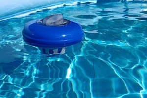 Close-up of a blue and white floating chlorine dispenser bobbing in bright, rippling swimming pool water for sanitization